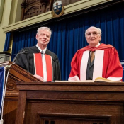 Photo of Larry Alford, a man with grey hair and a grey beard wearing a black academic gown and smiling, and Michael Walsh, a man with grey hair and glasses wearing a red academic gown, at Convocation Hall