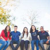 Five students sit on a concrete bench outside, each smiling at the cameral